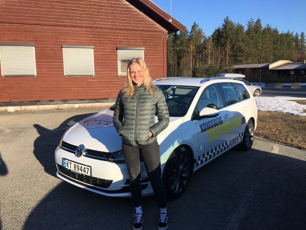 En person står foran en hvit skolebil med rutemønster og skolens navn